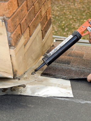 Chimney flashing repair project in New Jersey during clear weather with close-up of sealant application Chimney flashing repair project in New Jersey during clear weather with close-up of sealant application
